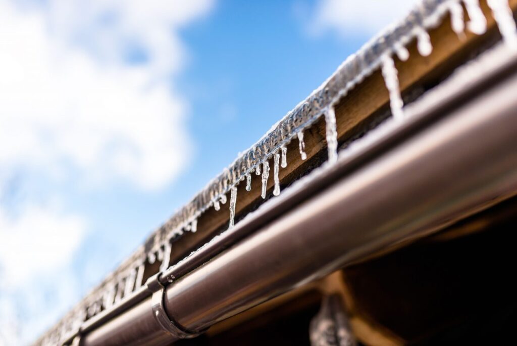 Gutters on brown roof with icicles hanging | horn brothers roofing Designing an effective gutter system